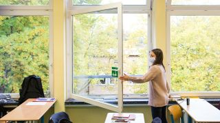 Symbolbild - Eine Schülerin mit einer Mund-Nasen-Bedeckung öffnet das Fenster ihres Unterrichtsraumes. (Bild: dpa/Daniel Bockwoldt)
