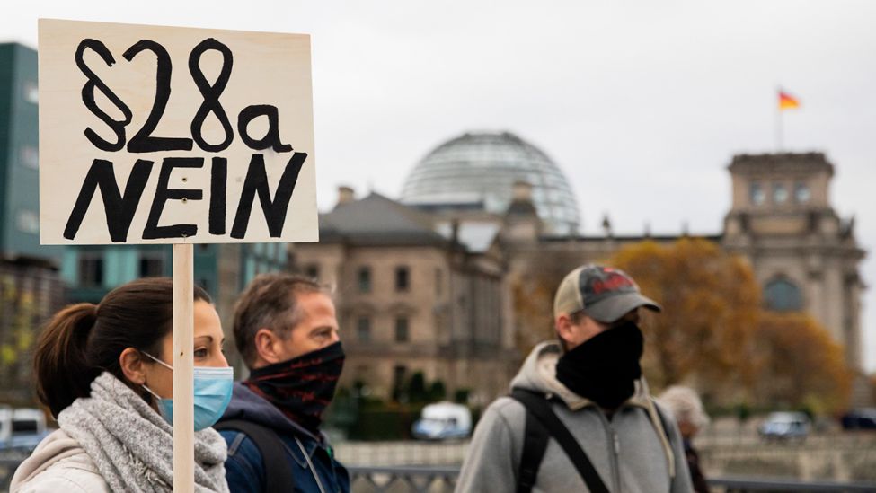 Teilnehmer einer Demonstration gegen die Corona-Einschränkungen der Bundesregierung stehen nahe dem Reichstagsgebäude auf der Marschallbrücke und halten ein Plakat mit der Aufschrift "Paragraf 28a NEIN". (Quelle: dpa/Christoph Soeder)