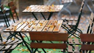 Leere Tische und Stühle stehen mit Herbstlaub bedeckt in einem Biergarten