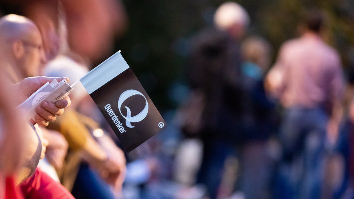 Ein "Q" und das Wort «Querdenker» stehen bei einer Kundgebung gegen die Corona-Maßnahmen am Brandenburger Tor auf dem Fähnchen eines Teilnehmers. (Quelle: dpa/Christoph Soeder)
