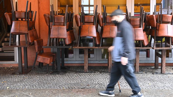 Ein Mann mit Mundschutz geht an einem Restaurant vorbei, vor dem die Stühle hochgestellt sind. (Quelle: dpa/Britta Pedersen)