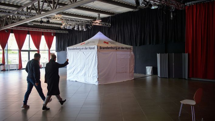 Zwei DRK-Mitarbeiter gehen im Foyer der Metropolishalle des Filmparks Babelsberg in Richtung des Zeltes, in dem ab 16.11.2020 der Corona-Abstrich bei Patienten gemacht werden soll. (Quelle: dpa/Soeren Stache)