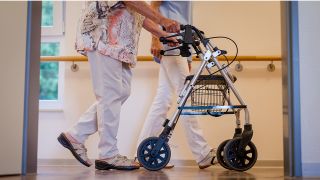 Eine Pflegekraft geht in einem Pflegeheim mit einer älteren Dame über einen Korridor. Quelle: dpa/Christoph Schmidt