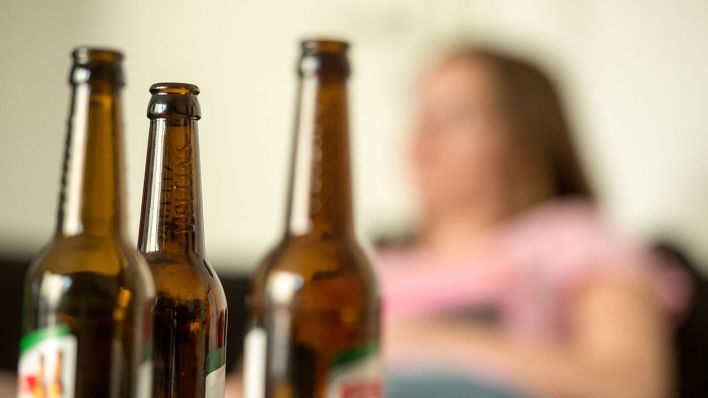 Illustration: Eine junge Frau sitzt hinter leeren Bierflaschen. (Quelle: dpa/Alexander Heinl)