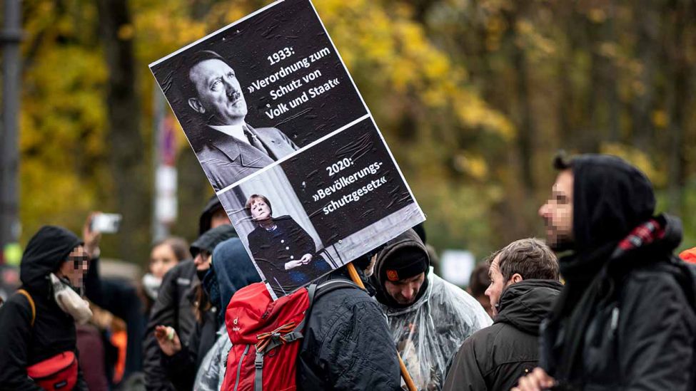 18.11.2020, Berlin: Ein Teilnehmer der Demonstration gegen die Corona-Einschränkungen hält ein Schild hoch auf dem unter Adolf Hitler Angela Merkel abgebildet ist (Quelle: Fabian Sommer/dpa)
