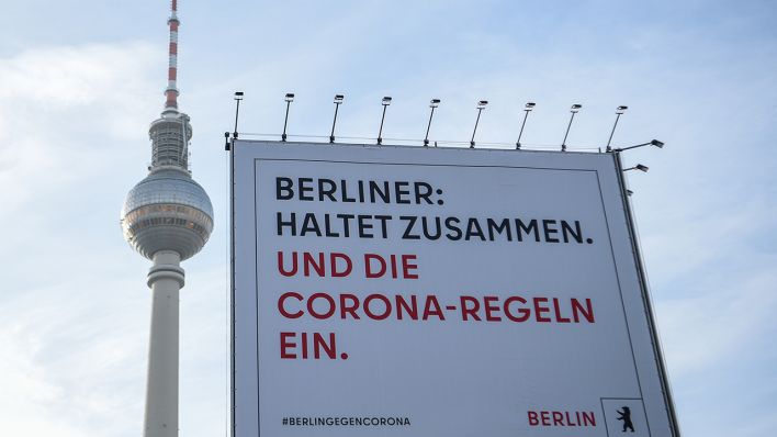 Vor dem Berliner Fernsehturm steht ein Plakat mit der Aufschrift „Berliner: Haltet zusammen. Und die Corona-Regeln ein.“ (Quelle: dpa/Kira Hofmann)