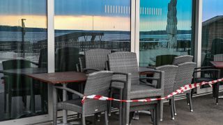 Abgesperrt sind Sitzplätze an einem Restaurant der Seepromenade, während sich in den Fenstern der Senftenberger See spiegelt. (Quelle: dpa/Patrick Pleul)