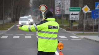 Mit einer Haltekelle regelt ein Polizist der Bundespolizei vor einem Grenzübergang den Fahrzeugverkehr. (Quelle: dpa/Stefan Sauer)