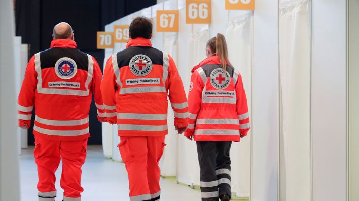 Mitarbeiter des Deutschen Roten Kreuzes gehen an den Impfkabinen des neuen Impfzentrums in der Arena Berlin vorbei. (Quelle: dpa/Hannibal Hanschke)