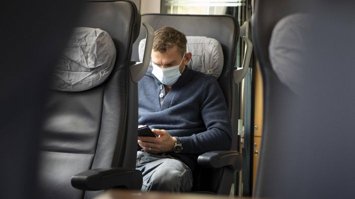 Symbolbild: Ein Mann sitzt mit Mund-Nase-Bedeckung an einem Vierertisch im ICE der Deutschen Bahn. (Quelle: imago images/U. Grabowsky)