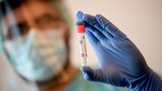 Symbolbild: Ein Arzt hält in einer Corona-Teststelle einen Abstrich für einen Coronavirus-Test in der Hand