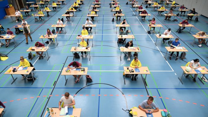 Schüler und Schülerinnen sitzen während der Deutsch-Abitursprüfung mit dem vorgeschriebenen Abstand zueinander in der Sporthalle eines Gymnasiums vor ihren Prüfungsaufgaben. (Quelle: dpa/Felix Kästle)