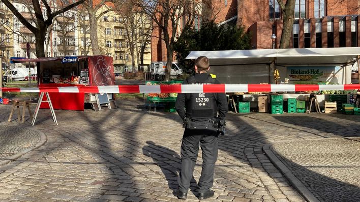 Ein Polizist steht hinter einem Absperrband auf dem gesperrten Wochenmarkt am Herrfurthplatz.