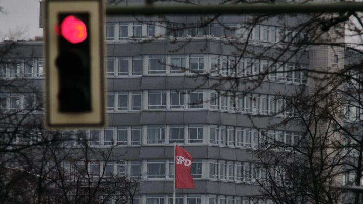 Eine Ampel steht auf Rot, während im Hintergrund die Fahne der Partei auf dem Dach der Parteizentrale der SPD im Wind weht. (Quelle: dpa/Stefan Jaitner)
