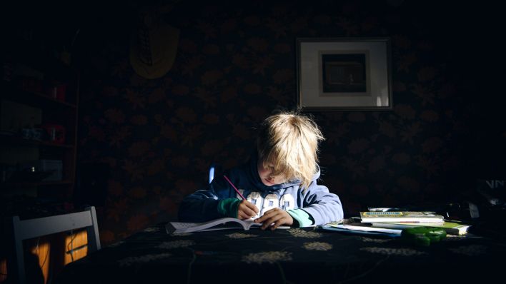 Ein Junge sitzt zu Hause an einem Tisch und schreibt in einem Schulheft. (dpa/Antti Aimo-Koivisto)