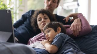 Eine Familie liegt auf einer Couch und sieht sich einen Film an. (Quelle: imago images/Joseffson)