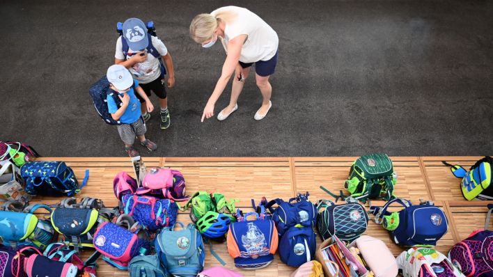 Eine Lehrerin zeigt zwei Erstklässlern in der Grundschule wo sie vor der ersten Stunde ihren Schultaschen auf einem Podest abstellen können. (Quelle: dpa/Soeren Stache)