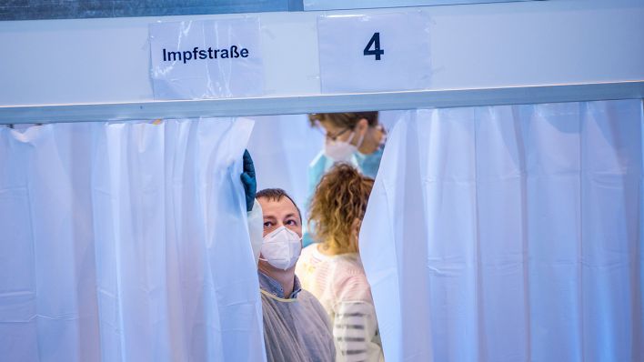 Ein Mitarbeiter schließt im Impfzentrum den Vorhang einer Kabine, in der gegen das Coronavirus geimpft wird. (Bild: dpa/Jens Büttner)