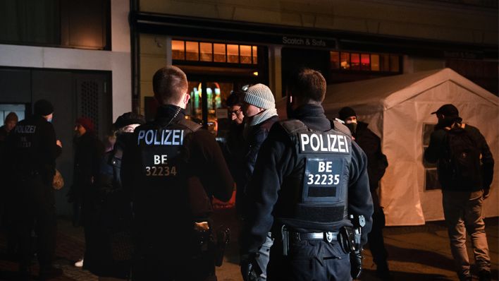 Polizisten und Passanten stehen am 14.01.2021 an der Kollwitzstraße vor einem gastronomischen Betrieb in Prenzlauer Berg (Bild: dpa/Paul Zinken)
