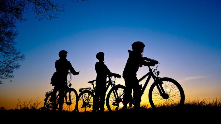 Eine Frau und ihre beiden Kindern auf Fahrrädern machen im Sonnenuntergang auf einem Radweg nahe Sieversdorf eine Pause, Archivbild (Quelle: DPA/Patrick Pleul)