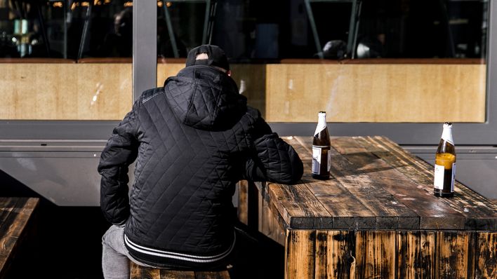Ein Mann sitzt auf einer Bank und trinkt Bier (Bild: dpa/Carsten Koall)