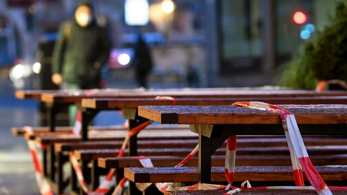 Symbolbild: Mit Absperrband umwickelt sind Tische und Bänke vor einer Bäckerei. (Quelle: dpa/Hendrik Schmidt)