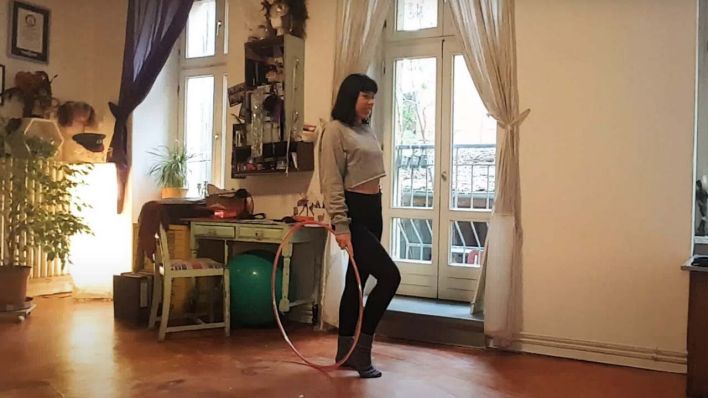 Hula-Hoop-Tänzerin steht in ihrem Wohnzimmer mit dem Reifen in der Hand / Dunja Kuhn