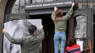 Ein Schild "Perspektive Kultur: Berliner Pilotprojekt Testing" wird im März 2021 über dem Eingang des Berliner Ensembles angebracht. (Quelle: dpa/Jens Kalaene)
