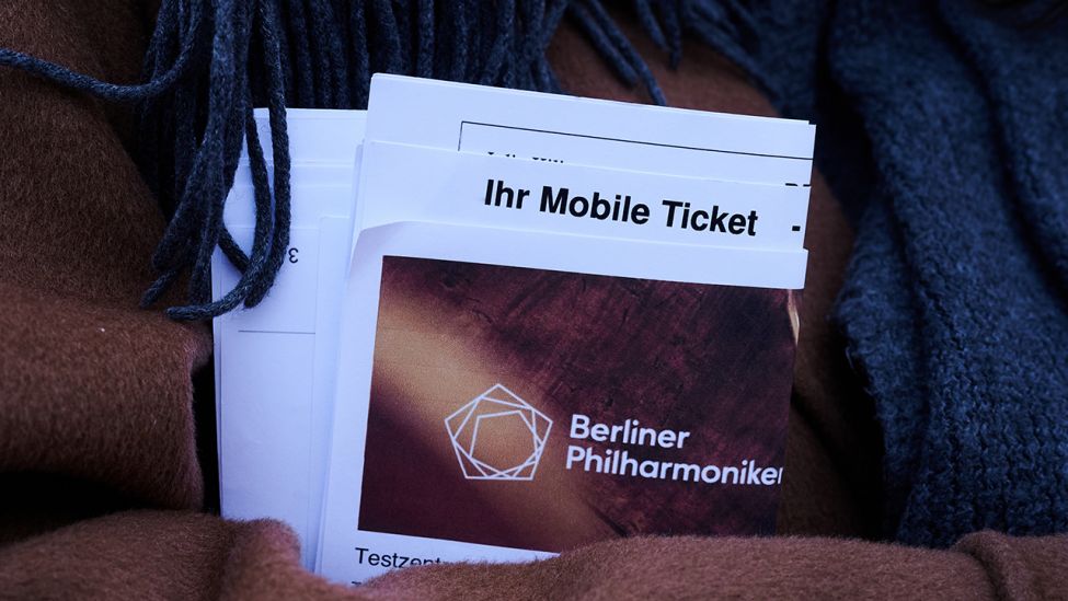 „Ihr Mobile Ticket“ und „Berliner Philharmonie“ steht am 20.03.2021 auf Papieren, die eine Besucherin vor dem Konzerthaus hält. (Quelle: dpa/Annette Riedl)
