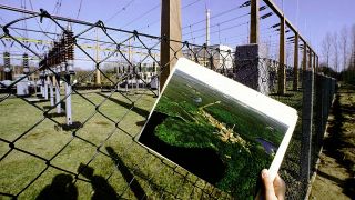 Hand hält Foto vom Kraftwerk Rheinsberg vor dem abgeschalteten Kernkraftwerk in Rheinsberg (Quelle: imago images)