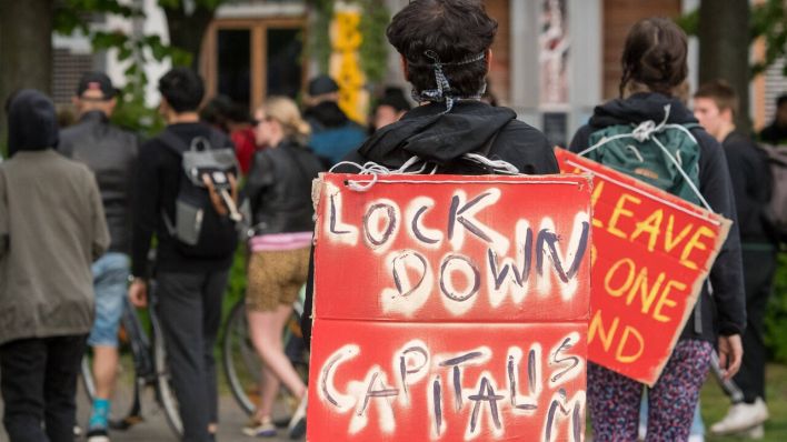 Im Bild ist eine Demonstrantin mit einem Schild mit lock down capitalism im Stadteil Kreuzberg zu sehen. (Bild: imago images/Christian Spicker)