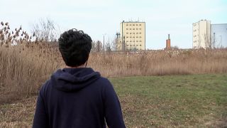 Ein Mann steht auf einem Feld in Sichtweite eines Fabrikgeländes (Bild: rbb)