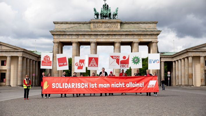 Teilnehmer einer Bild-Aktion des Deutschen Gewerkschaftsbundes (DGB) zum Tag der Arbeit halten vor dem Brandenburger Tor am 01.05.2020 (Bild: dpa/Christoph Soeder)