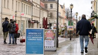 Ein Schild mit der Aufschrift „Betreten nur nach Vorlage eines negativen Corona-Tests“ steht vor dem Karstadt-Kaufhaus in der Einkaufsmeile Brandenburger Straße. (Quelle: dpa/Soeren Stache)