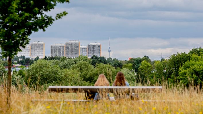 Symbolbild: Zwei Frauen sitzen auf einer Bank mit Sicht auf Plattenbauten und den Berliner Fernsehturm. (Quelle: dpa/Christoph Soeder)