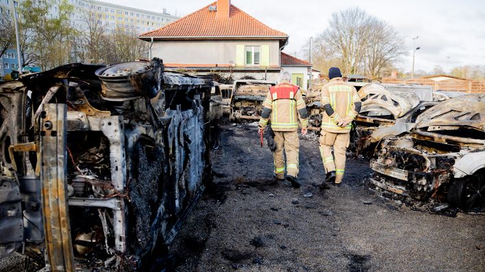 Feuerwehrmänner begutachten auf dem Gelände eines Autohauses in Berlin-Köpenick verbrannte Autos. Insgesamt hätten 14 Autos gebrannt, darunter auch Elektrofahrzeuge. (Quelle: dpa/Christoph Soeder)