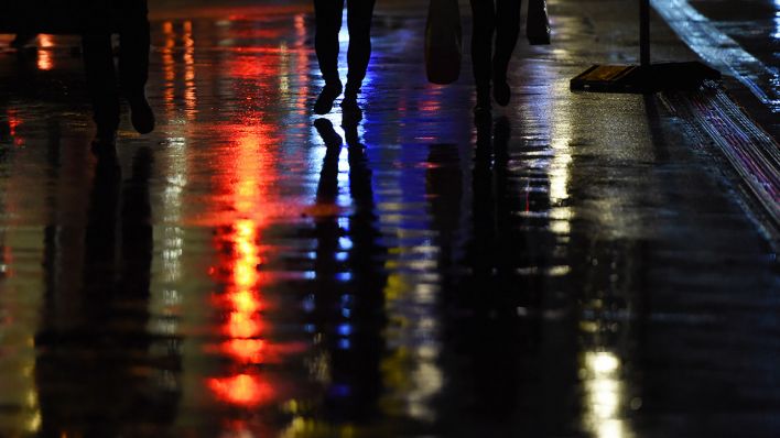Fußgänger gehen am 08.10.2015 in Berlin auf einem regenassen Gehweg am Abend bei Regen auf der Friedrichstraße, in der sich Lichter spiegeln. (Quelle: dpa/Jens Kalaene)