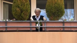 Eine Seniorin steht auf ihrem Balkon.