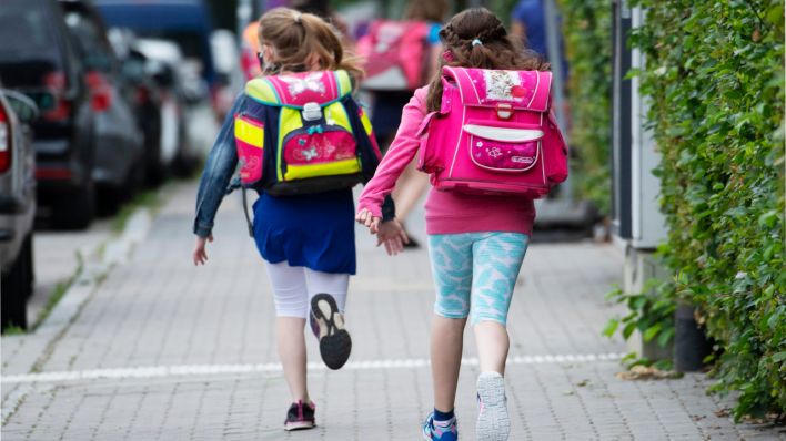 Zwei Schülerinnen einer Grundschule rennen mit einem Schulranzen auf dem Rücken die letzten Meter bis zum Schulhof. (Quelle: dpa/Boris Roessler)