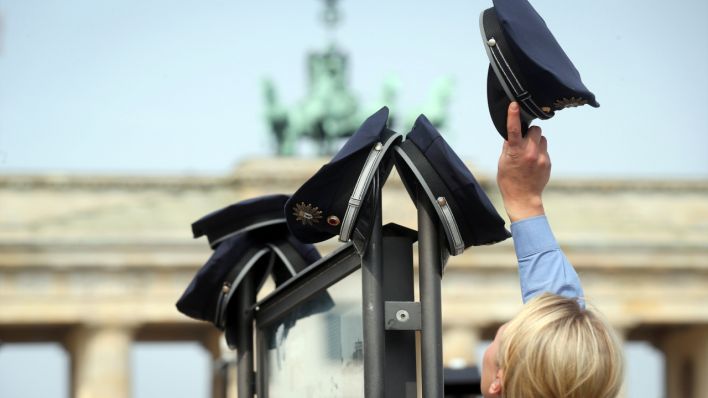 Mützen der Berliner Polizei hängen an einer Informationstafel in Berlin vor dem Brandenburger Tor (Quelle: dpa/Kay Nietfeld)