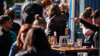 Menschen sitzen in der Sonne vor einer Bar in Berlin
