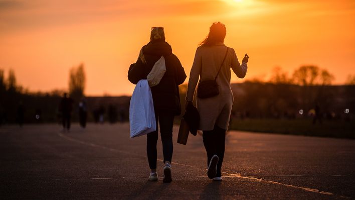 Zwei Frauen gehen auf dem Tempelhofer Feld während des Sonnenuntergangs spazieren (Bild: dpa/Christophe Gateau)