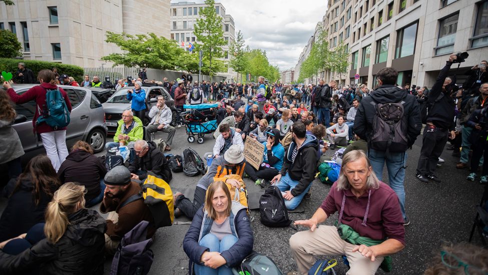 Teilnehmer einer Kundgebung gegen die Corona-Maßnahmen sitzen nahe dem Potsdamer Platz auf der Straße. (Quelle: dpa/C. Soeder)