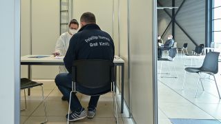 Eine Person itzt bei einem Gespräch im Impfzentrum der Bundeswehr und der Johanniter-Unfall-Hilfe e.V. am Flughafen BER. (Quelle: dpa/Patrick Pleul)