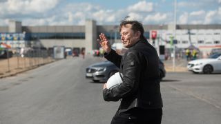 Elon Musk, Tesla-Chef, steht auf der Baustelle der Tesla Fabrik und winkt. (Quelle: dpa/Christophe Gateau)
