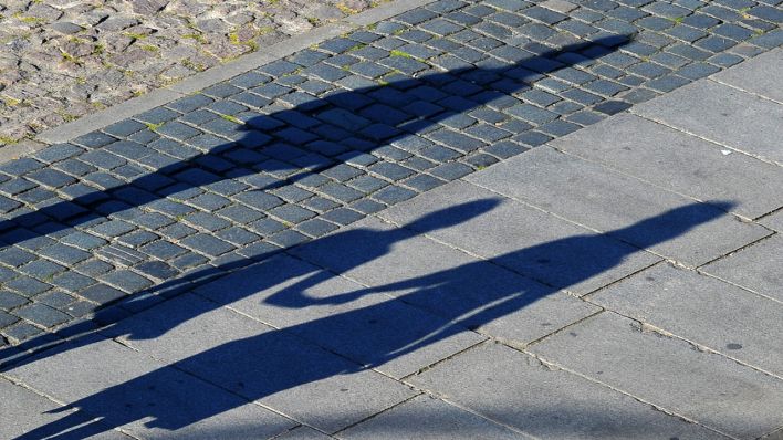 Symbolbild: Die Schatten zweier anonymer erwachsener Person und eines Kindes sind auf dem Pflaster einer Straße zu sehen. (Quelle: dpa/M. Hiekel)
