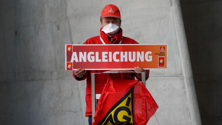 Ein unbekannter IG-Metall-Aktivist hält ein Schild hoch mit der Forderung "Angleichung"