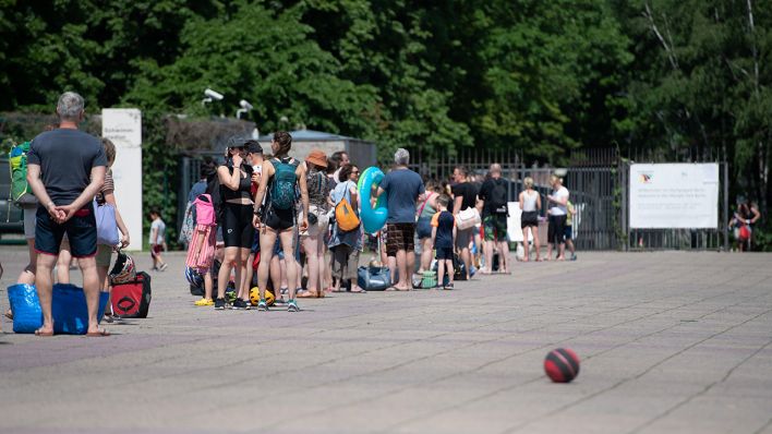 Menschen stehen bei warmem Wetter in einer Schlange vor dem Eingang zum Olympiabad in Berlin. (Quelle: dpa/Paul Zinken)