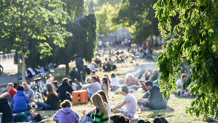 Zahlreiche Menschen sitzen im Licht der untergehenden Sonne auf einer Wiese im James-Simon-Park. (Quelle: dpa/Jens Kalaene)