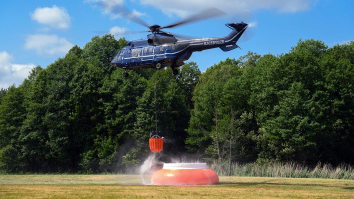 Ein Hubschrauber tankt auf der Lichtung eines Waldstücks Wasser zum Löschen nach. (Quelle: dpa/Soeren Stache)
